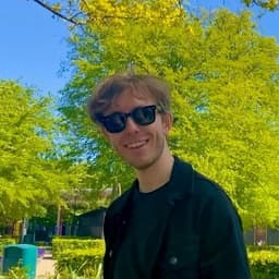 Portrait of me (Mikkel Bengtsen) on a sunny day smiling with black sunglasses on and lush green trees in the background.